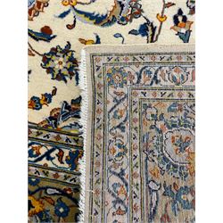 Persian Kashan ivory ground carpet, the field decorated with trailing foliate branches and stylised flower head motifs, guarded border with repeating design decorated with scrolling leafy branch and plant motifs 