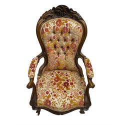 Victorian walnut framed open armchair, the pediment carved with flower heads and foliage, upholstered in buttoned floral fabric, shaped and carved arm uprights with scrolled terminals, on cabriole supports with brass castors