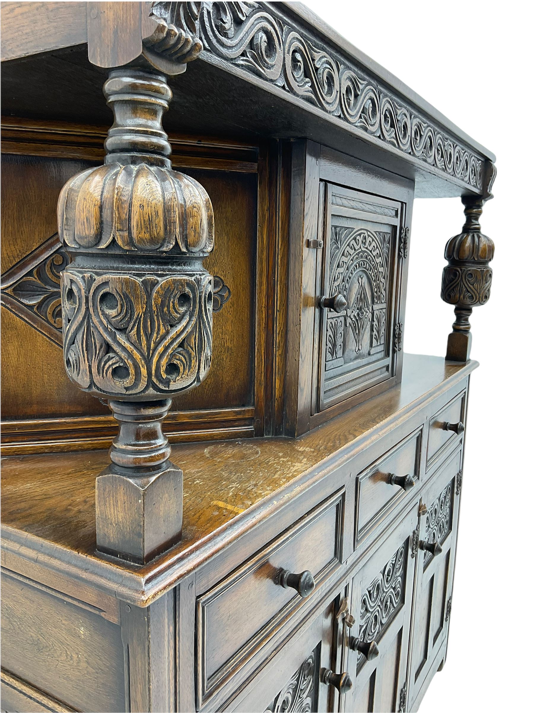 20th century carved oak court cupboard, s-scroll carved frieze over panelled cupboard door carved with arch, lobe and scroll carved cup and cover supports, fitted with three drawers and three cupboards below