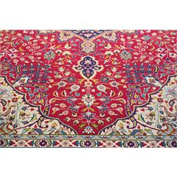 North West Persian Tabriz hand-knotted carpet, madder red field with a central cusped medallion issuing radiating pendants and an all-over design of scrolling arabesques, palmettes and flowering vinery enclosed by conforming spandrels, indigo main border of meandering floral vines and stylized palmettes, flanked by narrow guard stripes, cotton fringe ends 