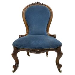 Victorian walnut spoon back nursing chair, the cresting rail carved with flower heads and trailing leafy branches, moulded framed carved with scrolled terminals, shell carved cabriole feet on brass and ceramic castors