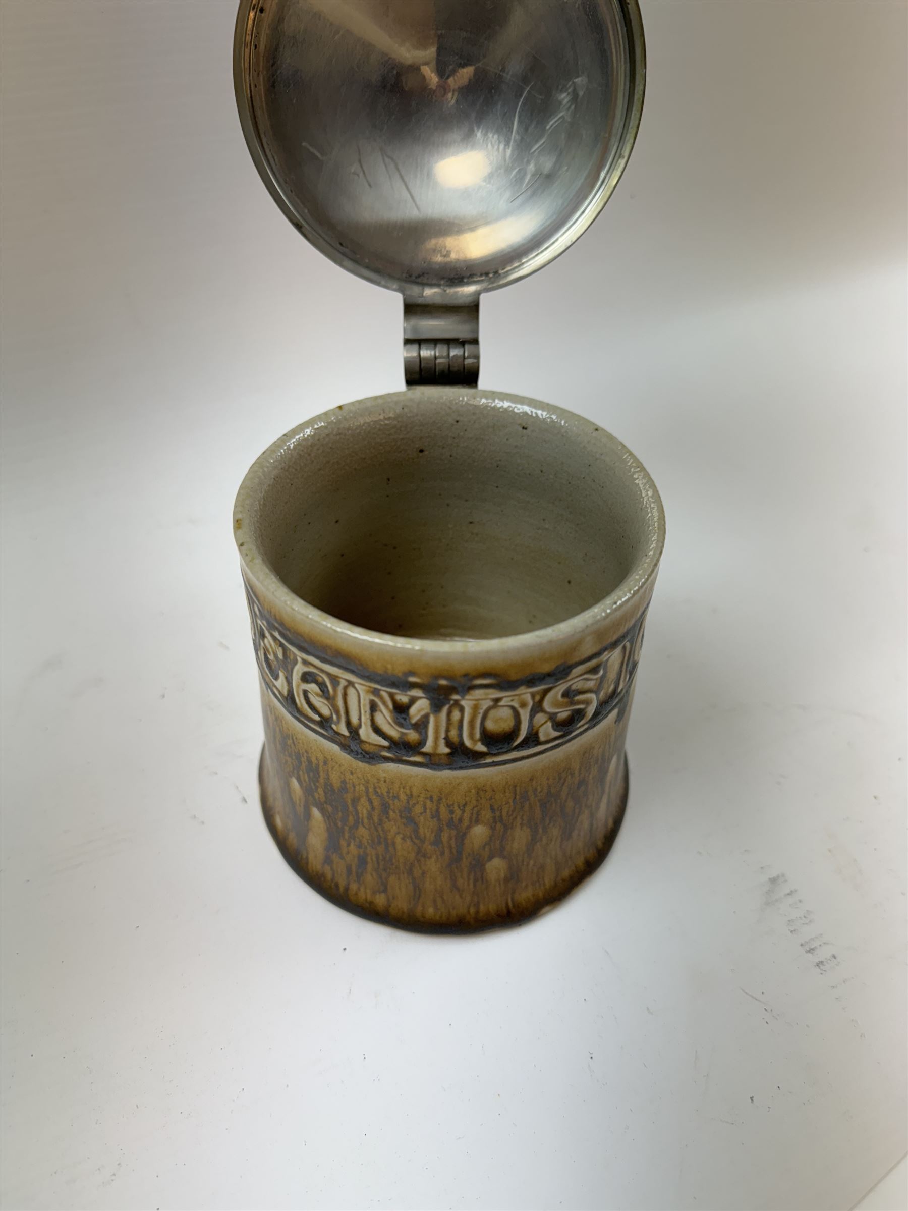 Arts and Crafts or Jugendstil tankard by Richard Riemerschmid, circa 1906, the cylindrical stoneware body reading 'Gaudeamus Igitur' (therefore let us rejoice), and finished in a brown glaze, with engraved slightly domed hinged lid, impressed mark beneath for Reinhold Merkelbach Grenzhausen, model number 2026 W, H14.5cm 