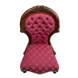 Victorian style mahogany framed nursing chair, the cresting rail carved with fruit and foliage, upholstered in red patterned fabric with buttoned back, on cabriole supports with scrolled terminals
