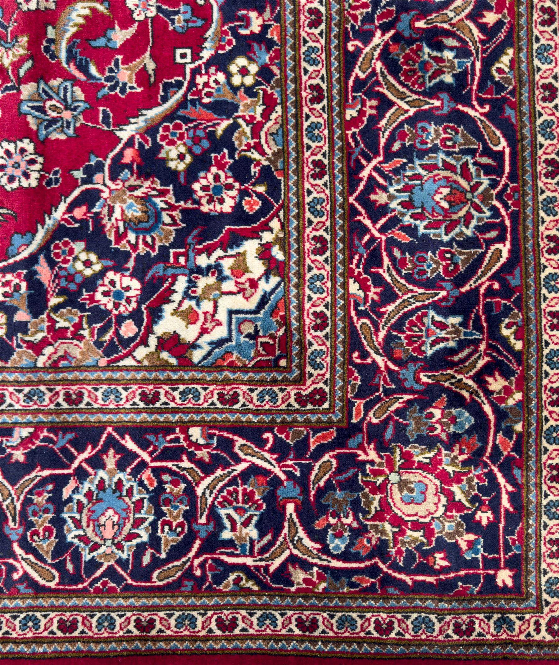 Central Persian Kashan hand-knotted carpet, the deep red ground with a central lozenge medallion in ivory and navy, surrounded by dense scrolling floral and vine motifs, navy spandrels and a wide border with stylised palmettes and flowerheads enclosed by multiple guard stripes