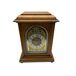 Jungans-German Edwardian 8-day oak cased mantle clock, with a stepped flat top and glazed door on a shallow plinth with bun feet, brass dial with cast spandrels, silvered chapter with Arabic numerals, chime/silent and pendulum regulation dials, three train spring driven movement sounding the quarters on gong rods and the hours on a coiled gong. With pendulum.