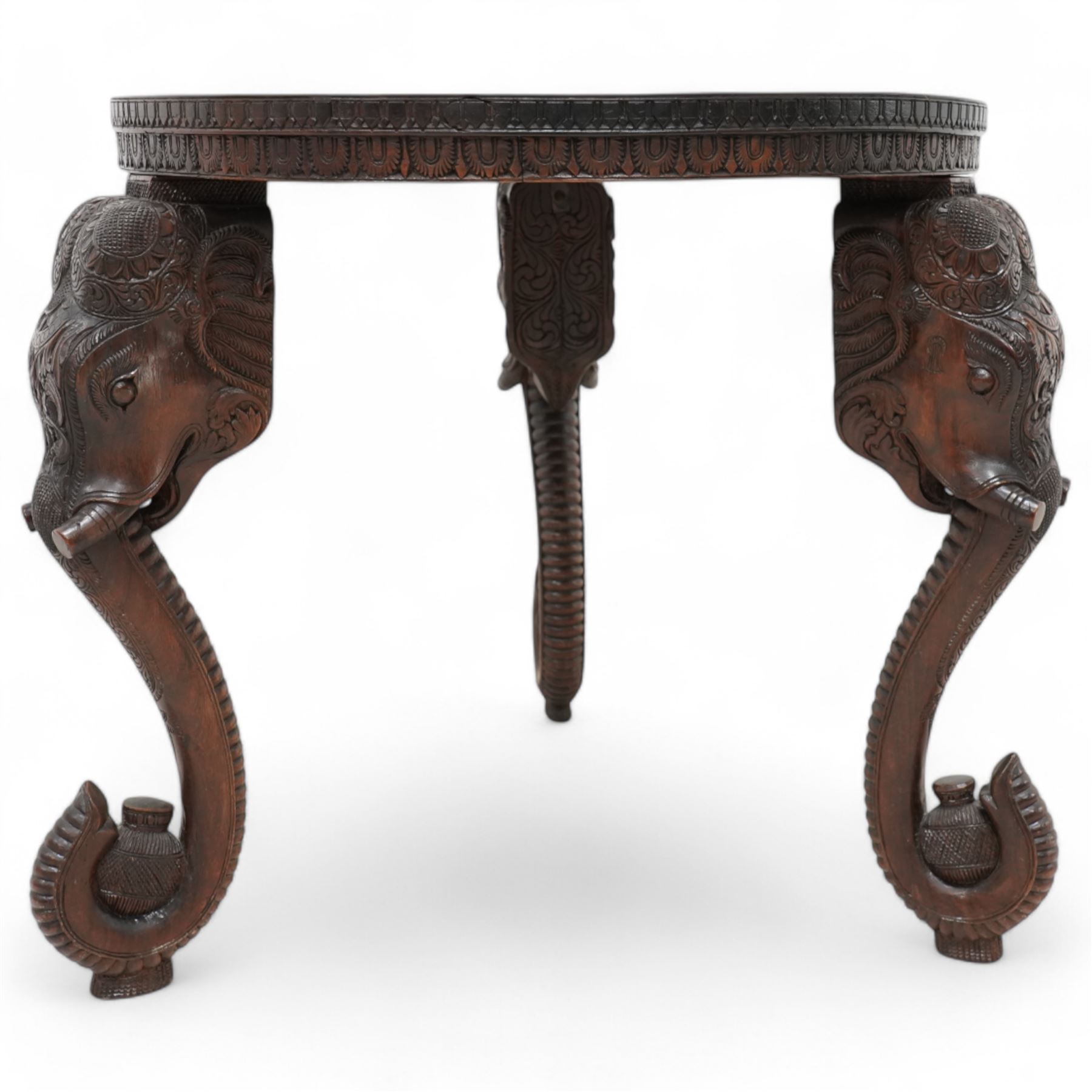 Anglo-Indian hardwood occasional table, circular top carved with concentric pattern and scrolling foliage, on three elephant carved supports decorated with flower heads