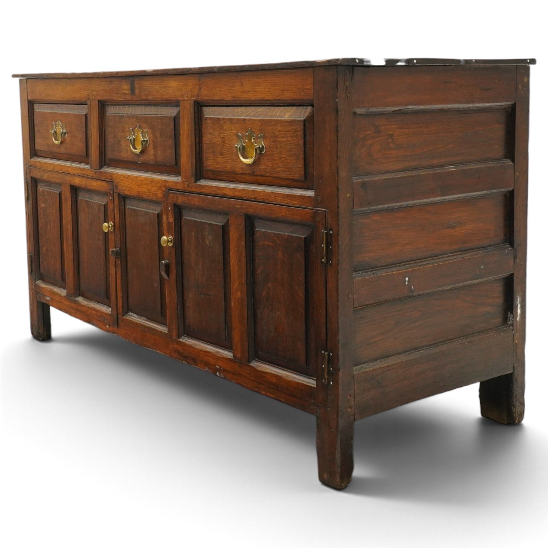 18th century oak dresser base, rectangular top over three drawers, fitted with twin panelled hutch-cupboard doors flanking central fielded panel, raised on stile supports