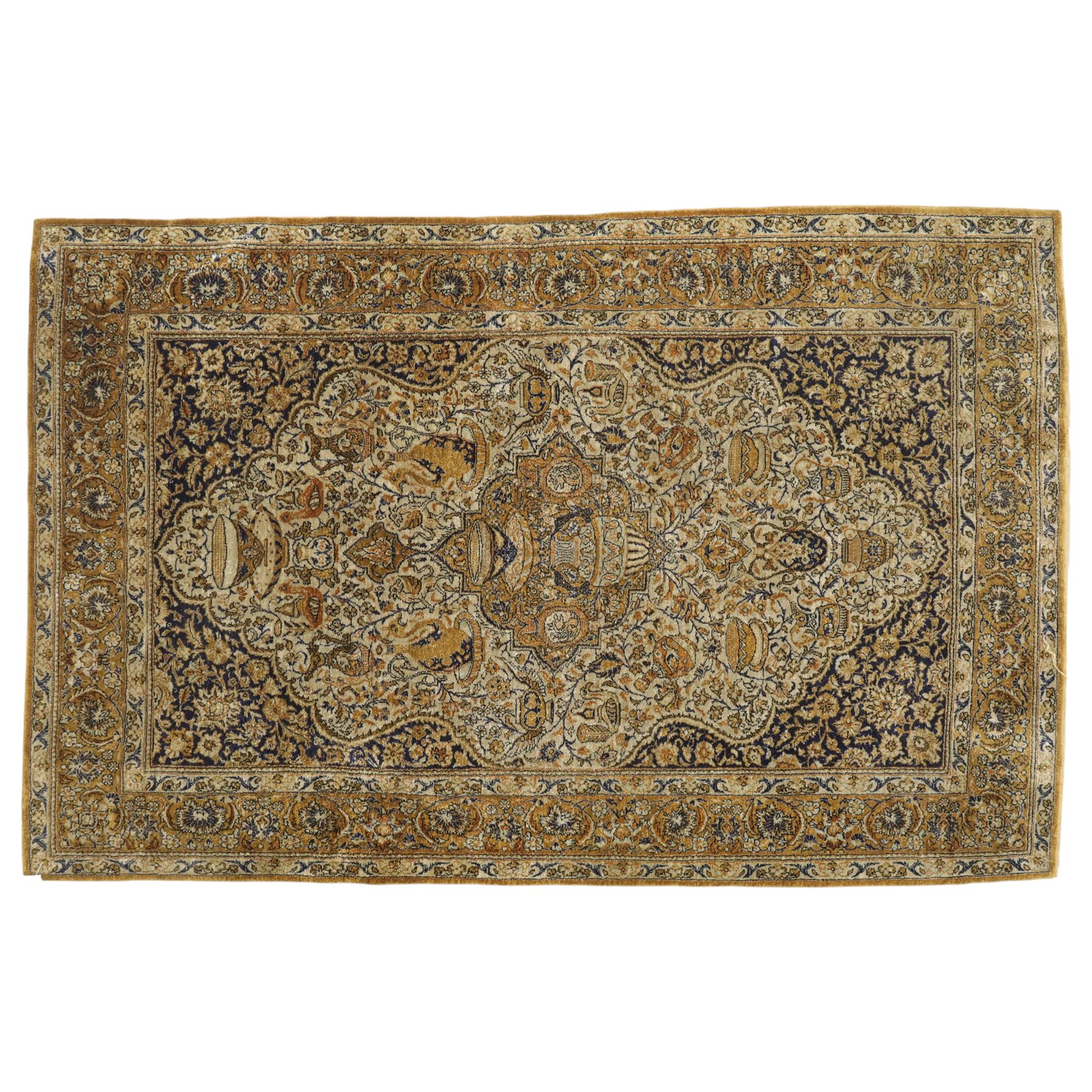 Persian Kashan design silk and wool blended rug, with a central medallion incorporating vases and scrolling floral motifs, set against a dark blue and ivory ground within a patterned border, some fraying to end fringes