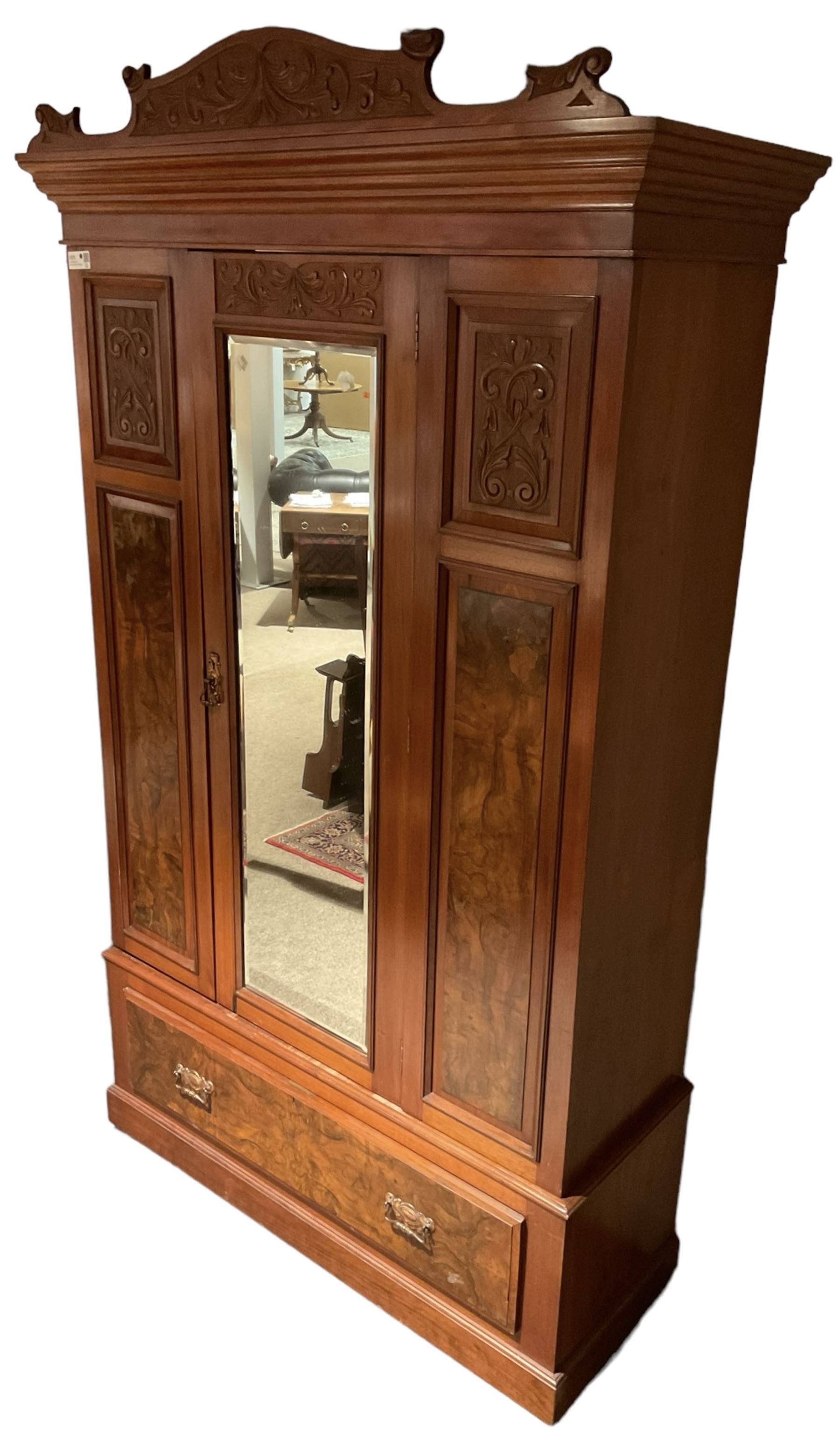 Late Victorian walnut wardrobe, carved arched pediment, fitted with single bevelled mirror door, flanked by carved and figured panels, enclosing hanging rail and hooks, single drawer fitted to base