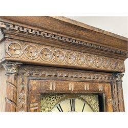 19th century carved oak longcase clock, projecting cornice over guilloche carved frieze, square brass dial with silvered Roman chapter ring and calendar aperture, decorated with ornate mask cast spandrels, the trunk door and base carved with potted plant, twin train driven eight day movement striking on bell