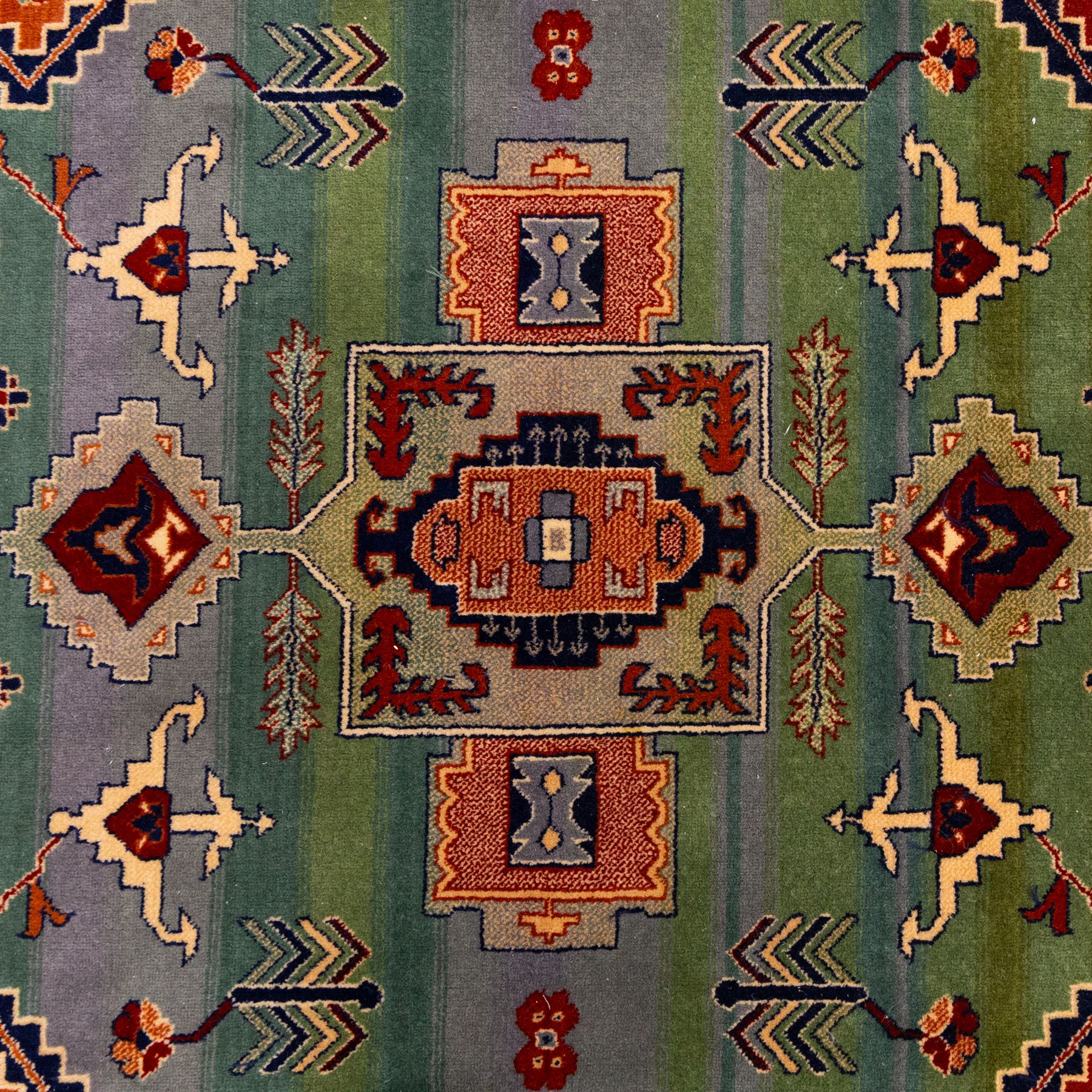 Late 20th century, French-made Caucasian design rug, woven with a dense pile, field decorated with a bold central stepped medallion flanked by stylized tribal and geometric motifs, borders of angular foliate designs in a palette of terracotta red with cotton fringe ends