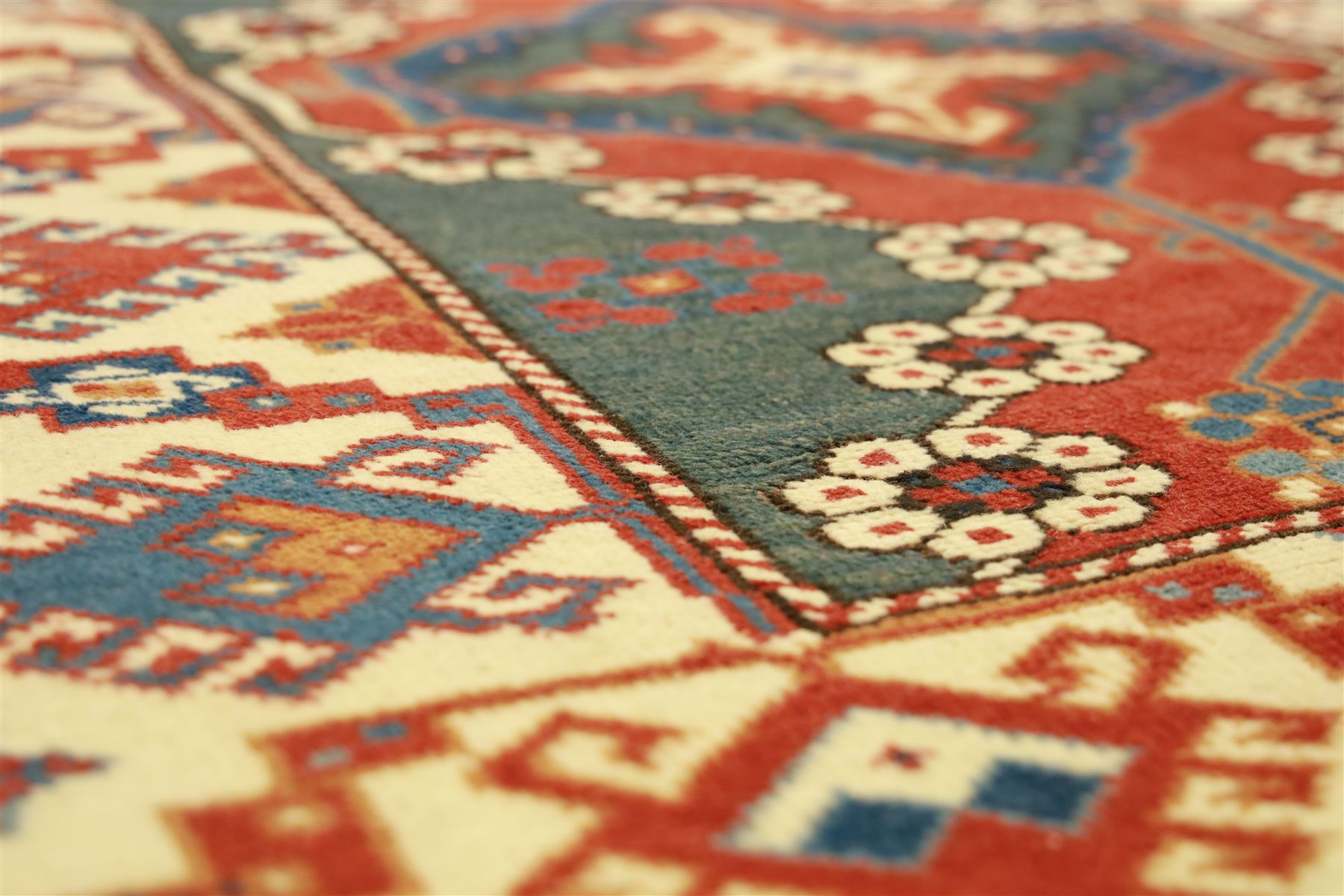 Caucasian Soumak rug, red madder field and teal panels, with bold stepped diamond medallion with hooked motifs and cruciform devices, and floral rosette clusters, surrounded by an ivory border with large hooked diamonds and stylized ram's horn devices, flanked by narrow guard stripes




