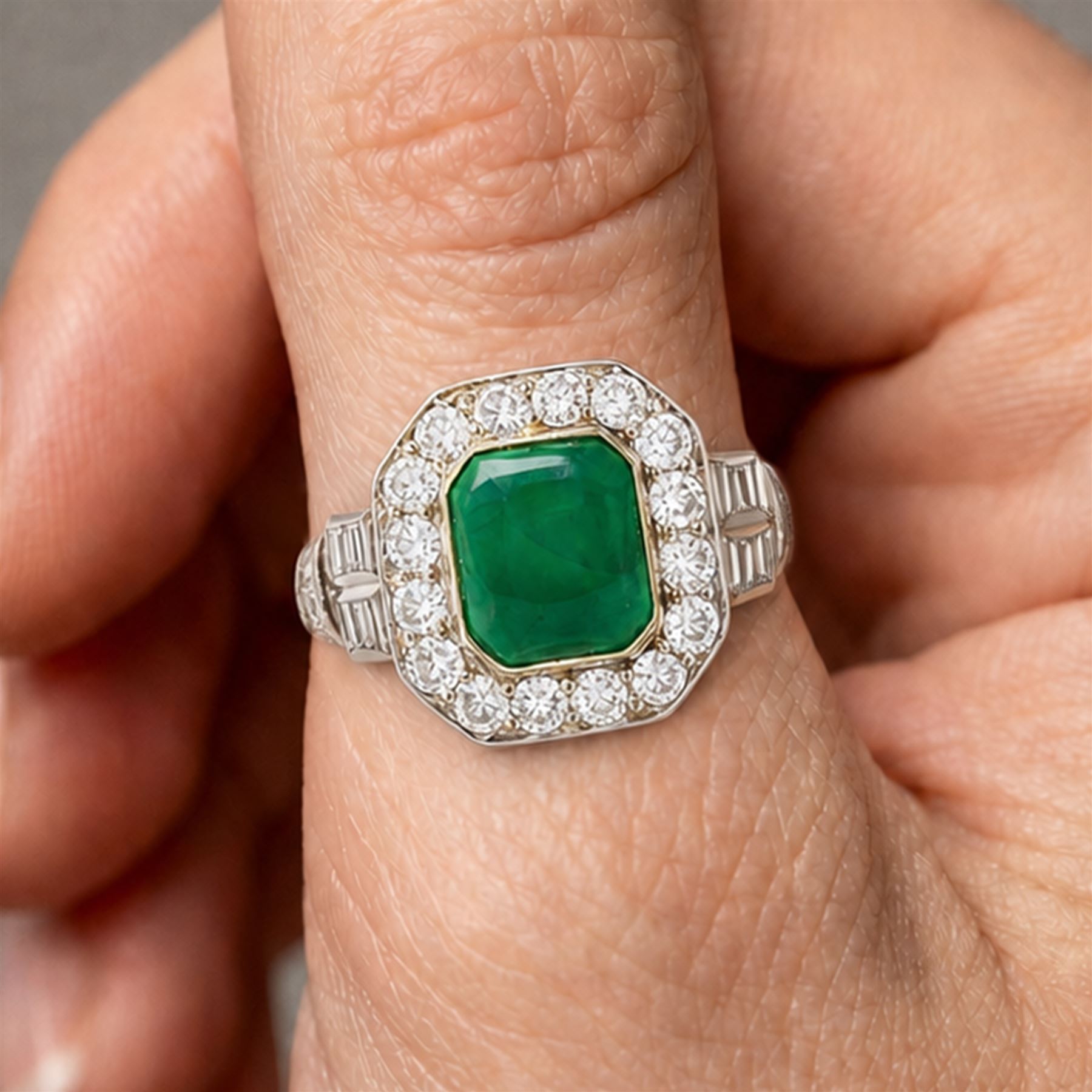 18ct white gold and platinum emerald and diamond cluster ring, single octagonal cabochon cut emerald, surrounded by sixteen milgrain set round cut diamonds, the shoulders set with baguette and single cut diamonds, stamped 18ct, total diamond weight approx 1.55 carat