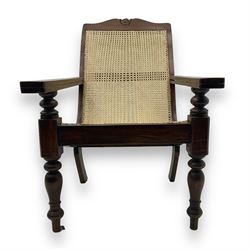 Late 19th century caned plantation chair, shaped top rail with carved central motif over caned back and seat, extending armrests, on turned front supports
