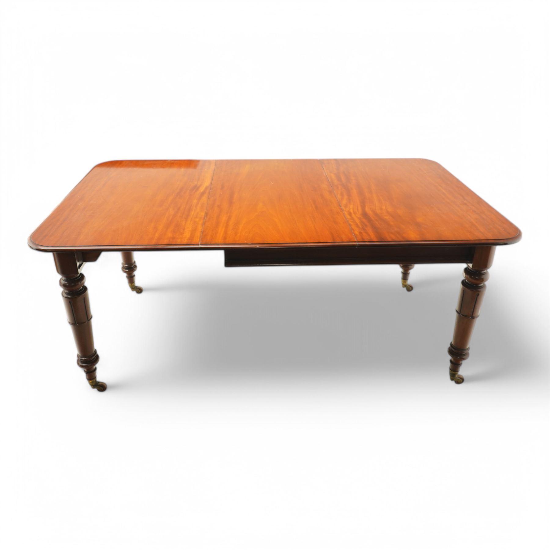 Victorian mahogany extending dining table, moulded rectangular top with rounded corners, pull-out action with additional leaf, on turned and lappet carved supports terminating to brass and ceramic castors 