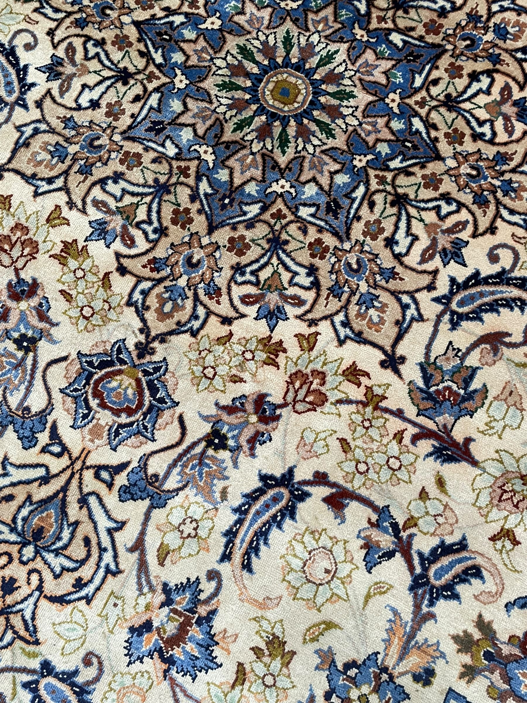 Persian Kashan ivory ground carpet, floral design central medallion surrounded by trailing and interlaced leafy branches with palmettes and flower heads, matching patterned border with guard stripes 