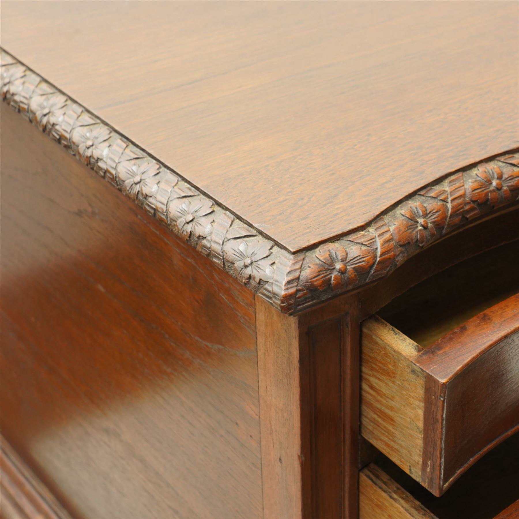 20th century oak and mahogany serpentine chest, the moulded top carved with trailing crossed ribbon and flower heads, fitted with three long cock-beaded drawers, ornate cast gilt metal handles, on acanthus leaf carved cabriole supports with ball and claw feet 