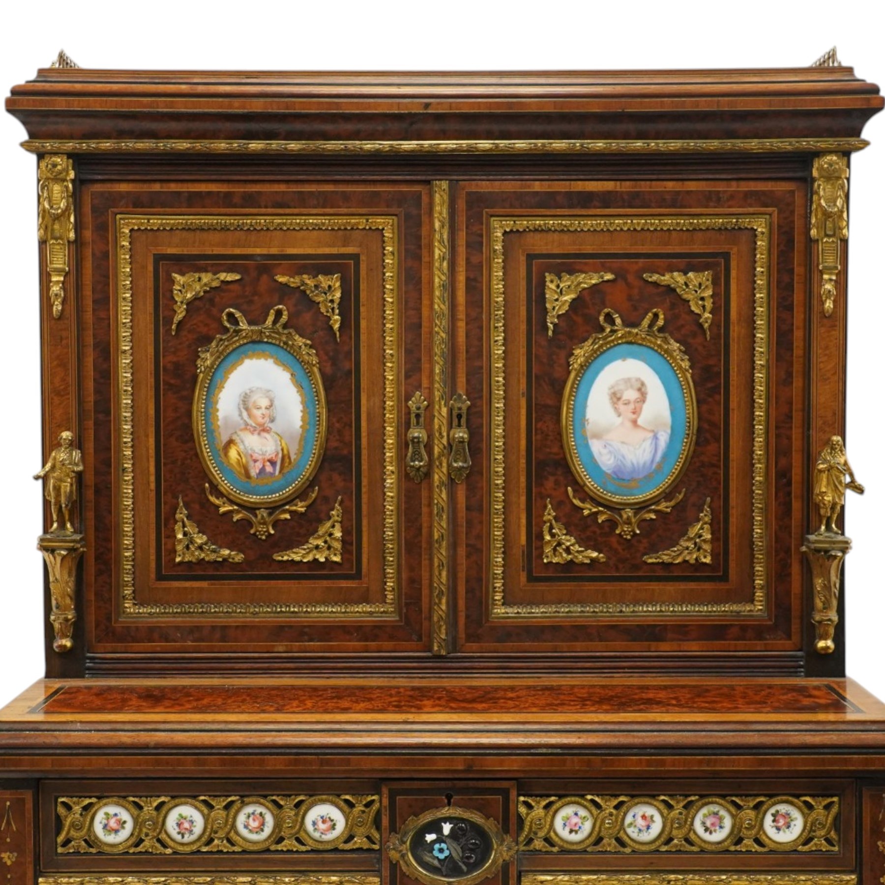 Fine late 19th century Aesthetic Movement ebony and amboyna cabinet on stand with parcel-gilt detail, the moulded cornice with pierced gilt-brass three-quarter gallery above a pair of panelled doors centred by oval porcelain portrait plaques within gilt-metal ribbon-tied frames, the doors further enriched with gilt-metal foliate mounts and flanked by classical figural terms, enclosing a shelved interior, the projecting lower section with amboyna top above a frieze drawer set with a series of floral porcelain roundels within pierced gilt-metal mounts and a central oval floral plaque, raised on turned and fluted supports with gilt-heightened detail, the mirrored back behind two amboyna shelves with pierced gilt-brass galleries, on turned feet