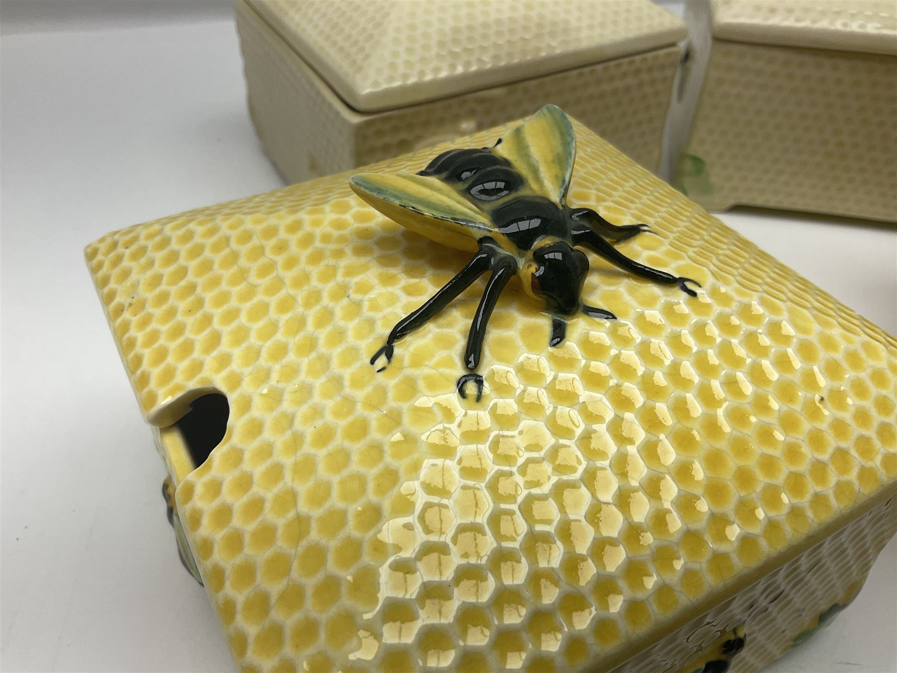 Four square honey boxes with lids,  each decorated with honeycomb pattern and finished with a bee finial