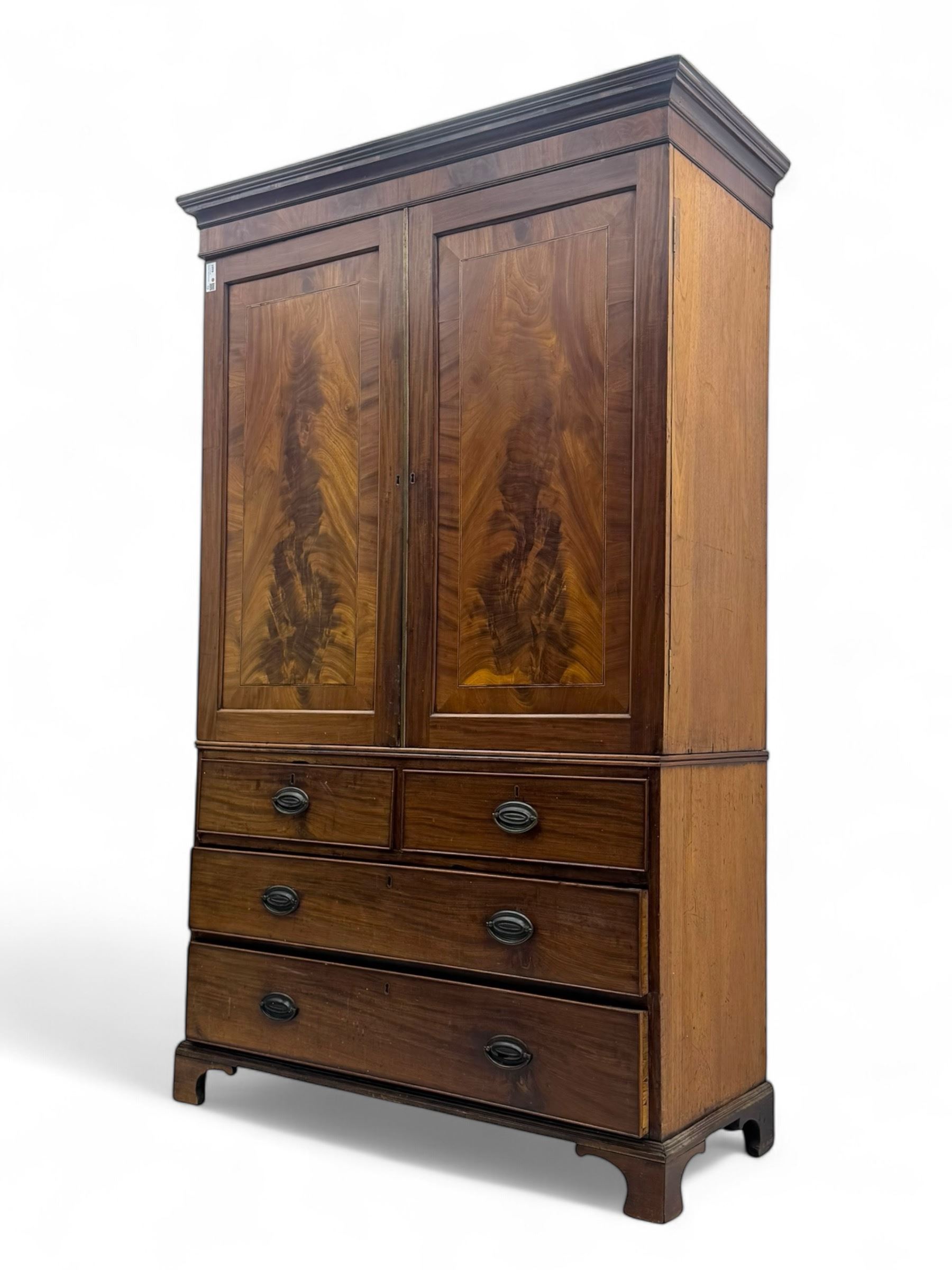 Early 19th century mahogany linen press cupboard, projecting moulded cornice over figured frieze, two panelled doors enclosing shelves, fitted with two short and two long cock-beaded drawers, on bracket feet 