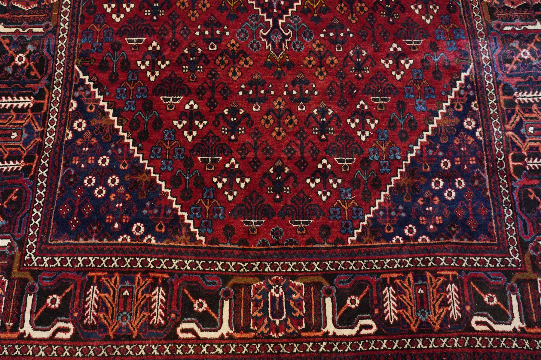 Central Persian Joshaghan hand-knotted carpet, deep red field decorated with a lattice design of stylized boteh and palmette motifs arranged around a stepped diamond medallion, navy corner spandrels similarly decorated enclosed by a dark indigo main border of floral and geometric motifs between multiple guard stripes, with cotton fringe ends 