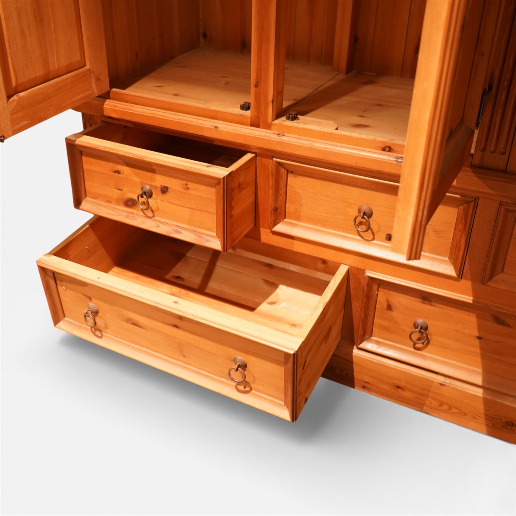 20th century pine wardrobe with drawer base, moulded cornice over three fielded panel cupboard doors enclosing hanging compartments, the base fitted with three short and two long drawers with brass ring handles, raised on a plinth base
