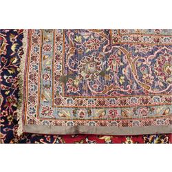 Persian Kashan hand-knotted carpet, madder red ground centred by shaped dark navy and ivory floral medallion with pendants, surrounded by scrolling vines, palmettes and flowerheads, dark navy spandrels, enclosed by dark navy floral border with multiple narrow floral guard stripes