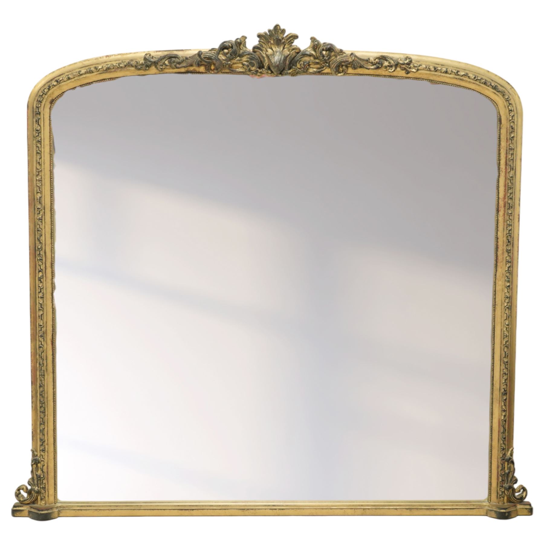 Regency style gilt overmantle mirror, arched rectangular frame with moulded surround, surmounted by a central anthemion and scrolling foliate crest, the frame enriched with beaded and foliate mouldings, the lower corners with applied scroll terminals, enclosing a single rectangular mirror plate