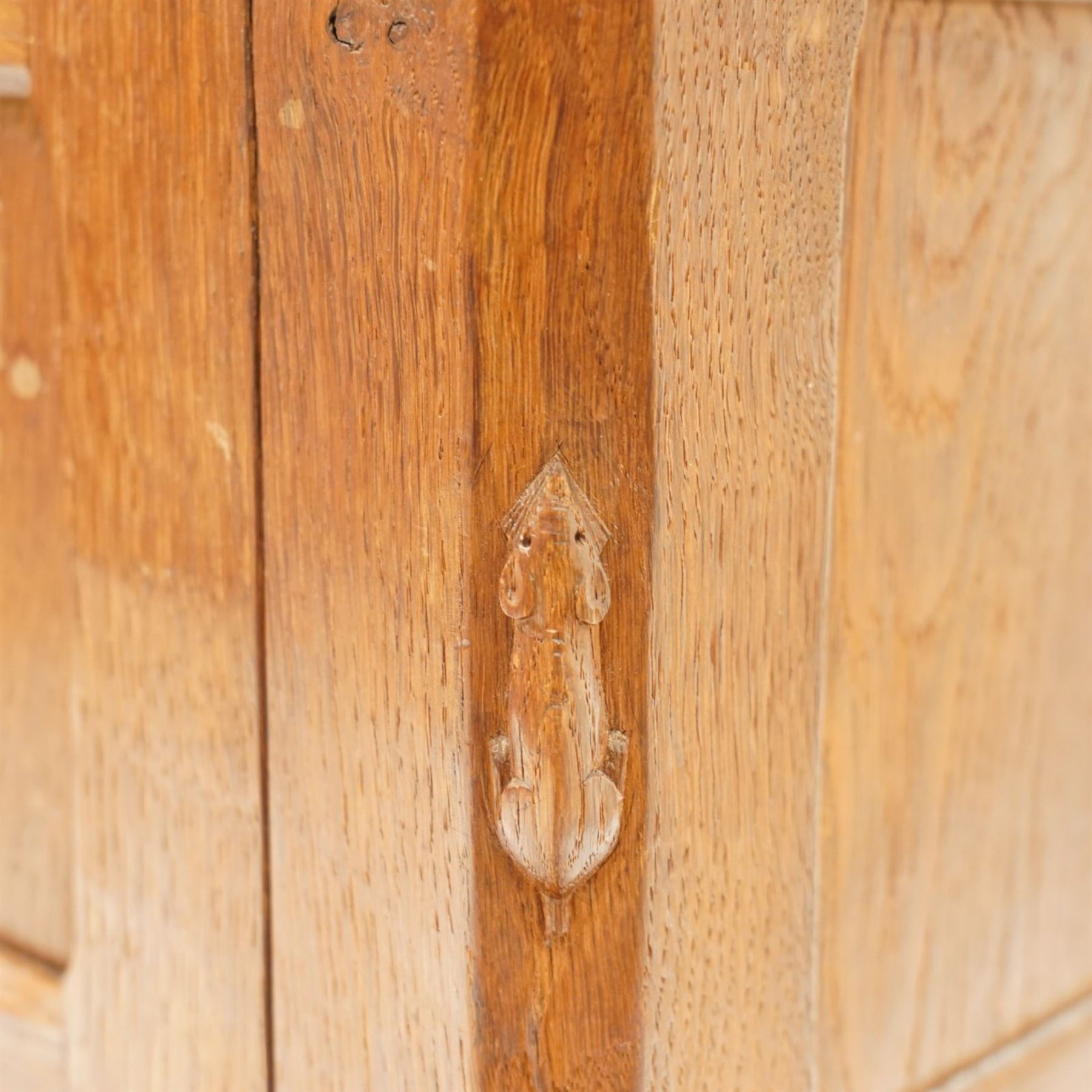 Mouseman - early-to-mid-20th century adzed and panelled dark oak bedside cupboard, raised back over rectangular canted top, fitted with single panelled cupboard door with chamfered rails and wrought iron fittings, enclosing two adjustable shelves, raised on canted square feet, carved with mouse signature, by the workshop of Robert Thompson of Kilburn