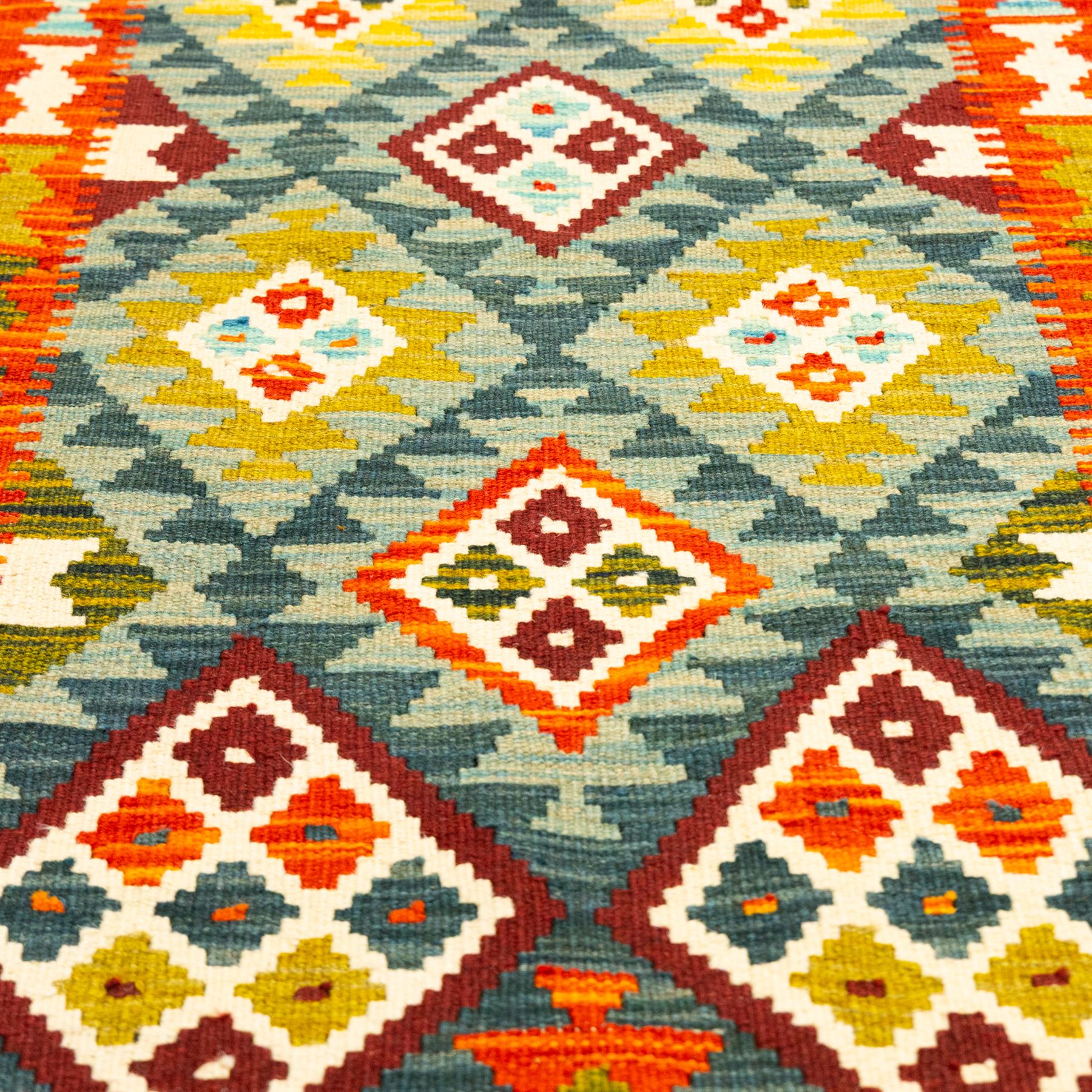 Afghan Maimana kilim flatweave runner, central field features a large bold nested diamond motifs and stylized geometric lozenge patterns on crimson, olive purple, blue, and green tone ground, border stripe in teal ground, and fringe
