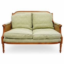 French Empire design varnished wood three piece lounge suite comprising of two cane armchairs and matching sofa, carved top rails with foliate terminals, cane side panels and padded scroll arms, upholstered in a green brocade with matching piping, on fluted legs