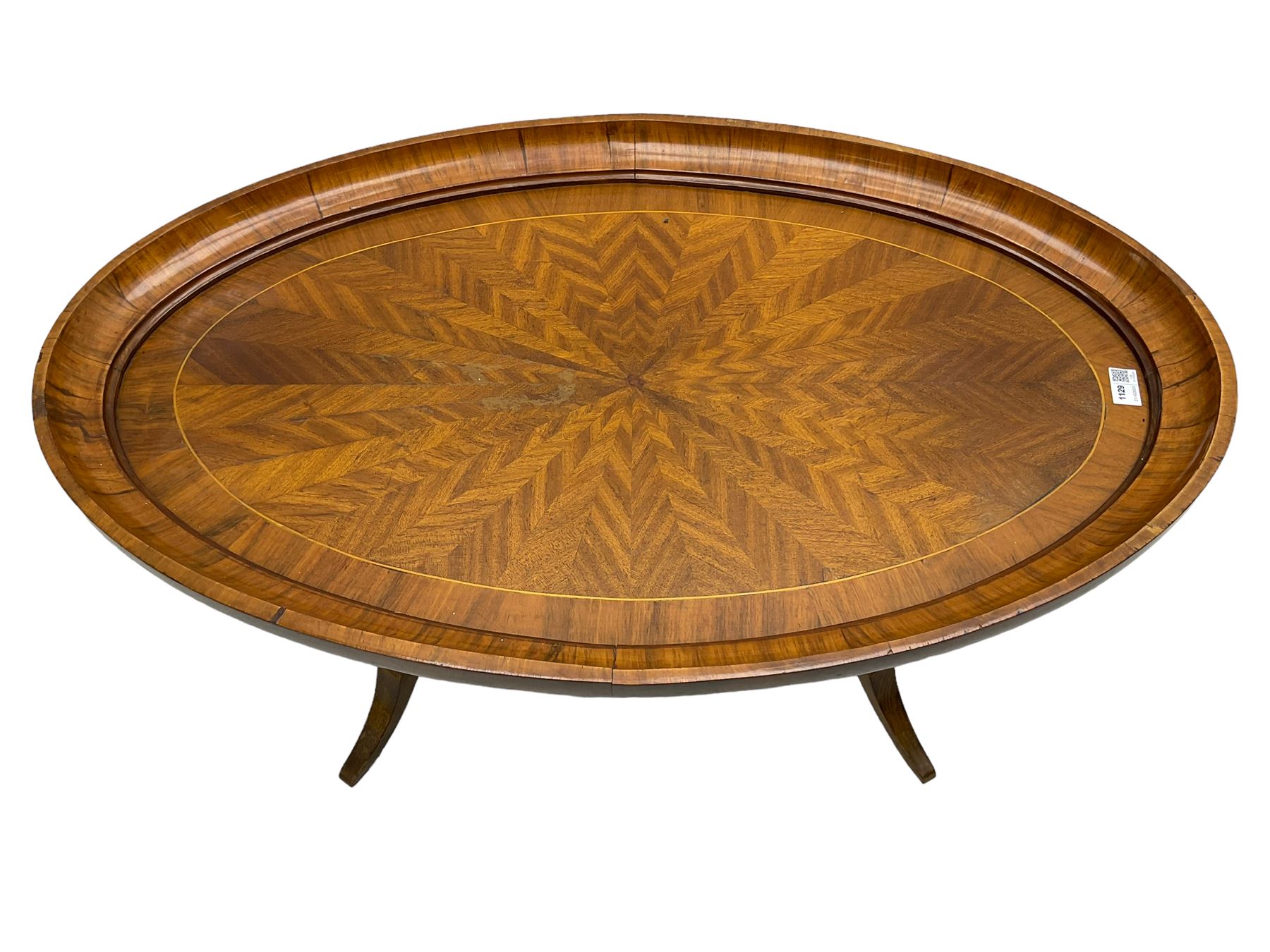 Early 20th century walnut coffee table, oval dished top with sunburst matched veneer, raised on twin cluster columns united by turned stretcher base on splayed supports