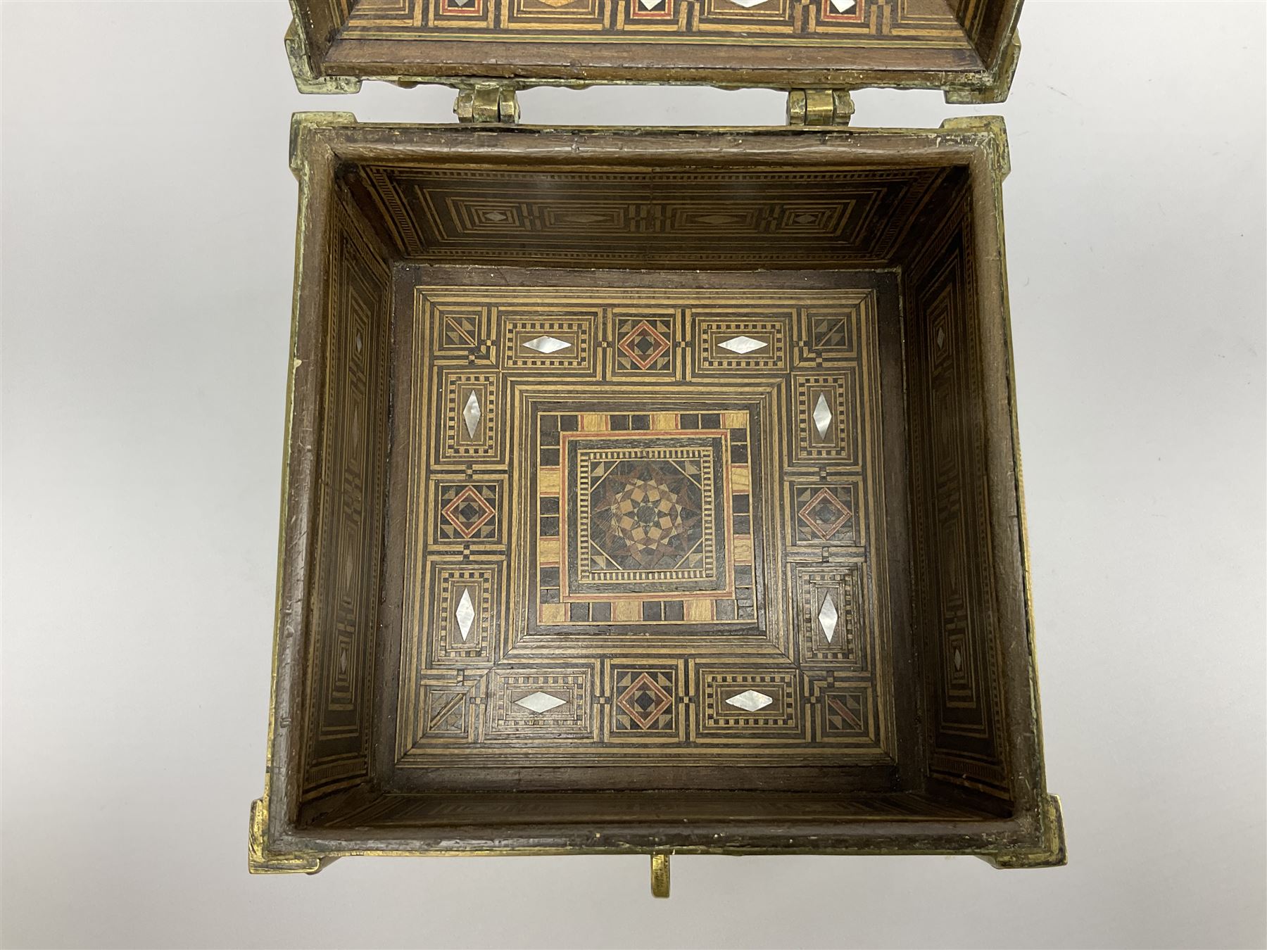 Late 19th century Damascus Cairoware Quran box, of square form with canted hinged cover, upon four circular pad feet, the brass exterior inlaid with silver and copper script and decorative detail, opening to reveal a marquetry lined interior, H15.5cm W19cm D19cm