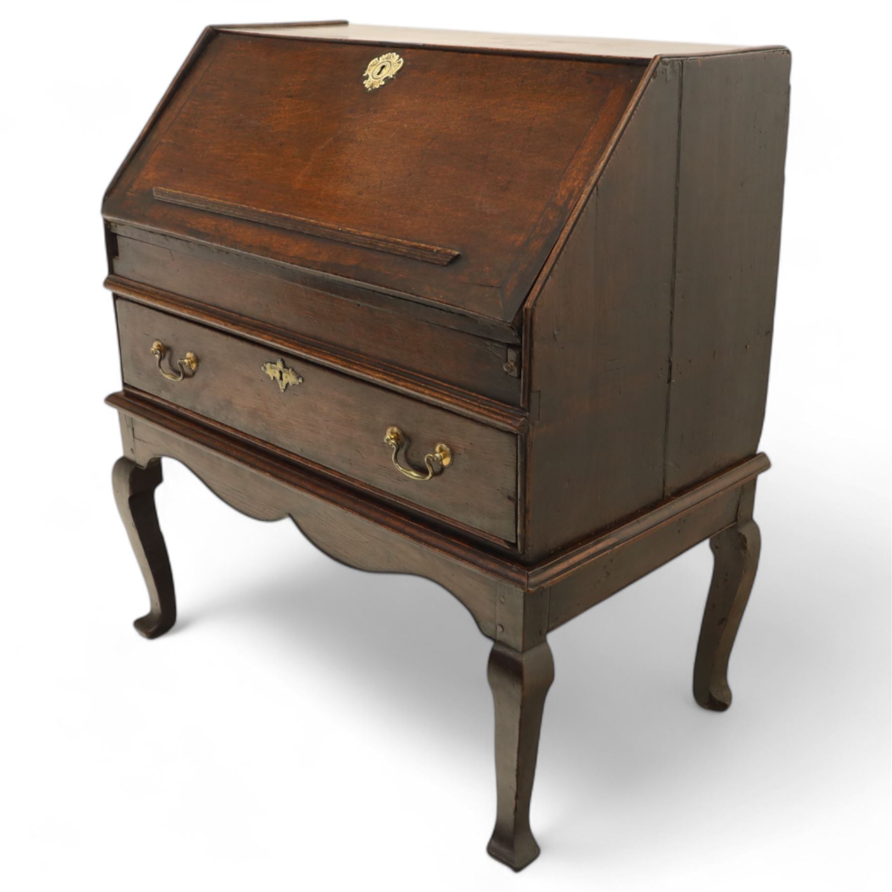 Early 18th century George I oak bureau on original stand, the fall front enclosing an arrangement of correspondence drawers and pigeonholes over central well, fitted with single long drawer below, the shaped apron over cabriole supports with pad feet
