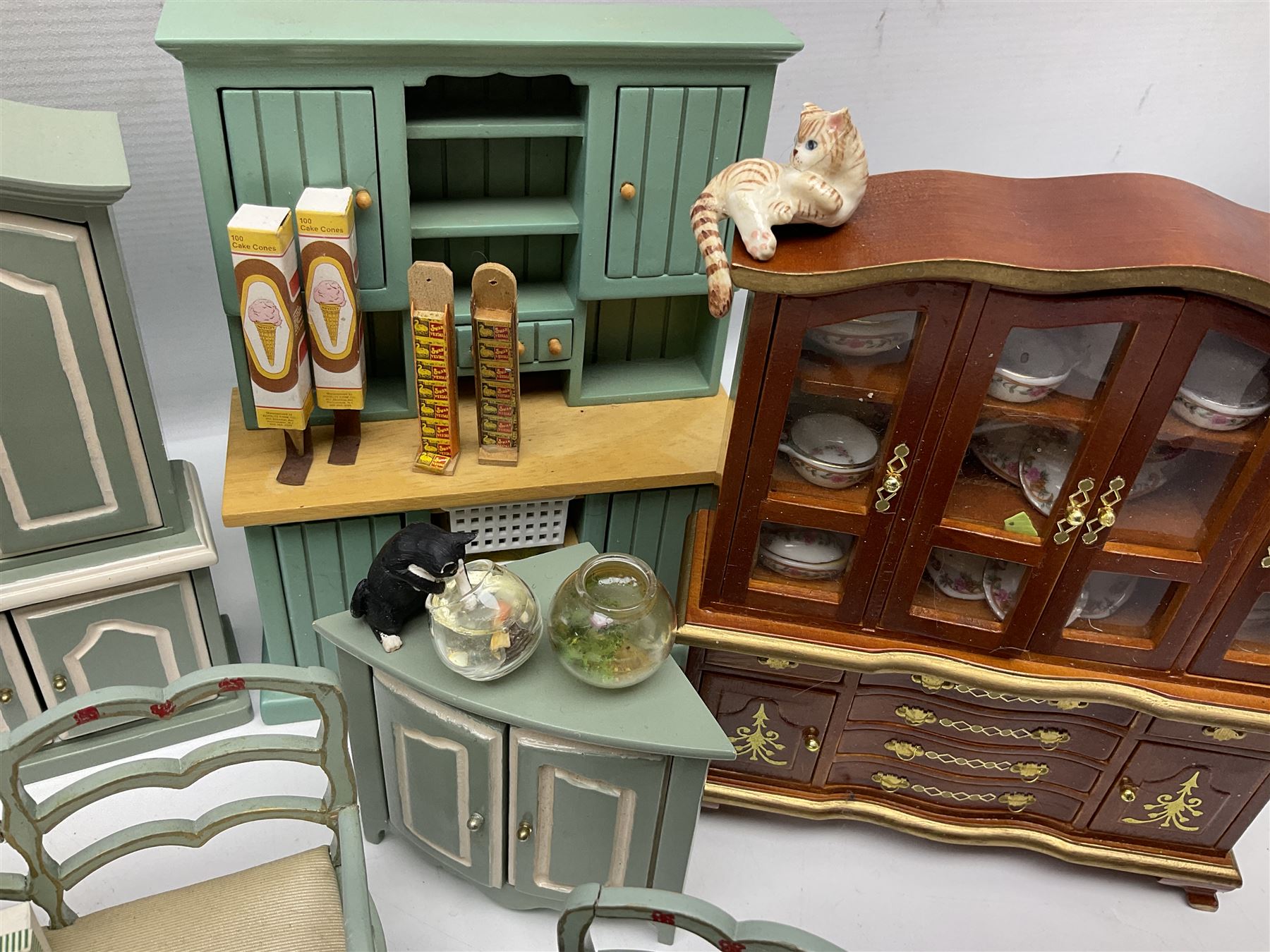 Collection of miniature dolls house furniture, to include display cabinet with pink and white floral dinner service, two serving trolleys with cakes and sweets and two blue painted kitchen dressers, together with miniature dolls house cardboard food packaging and animal figures including dogs and cats, etc