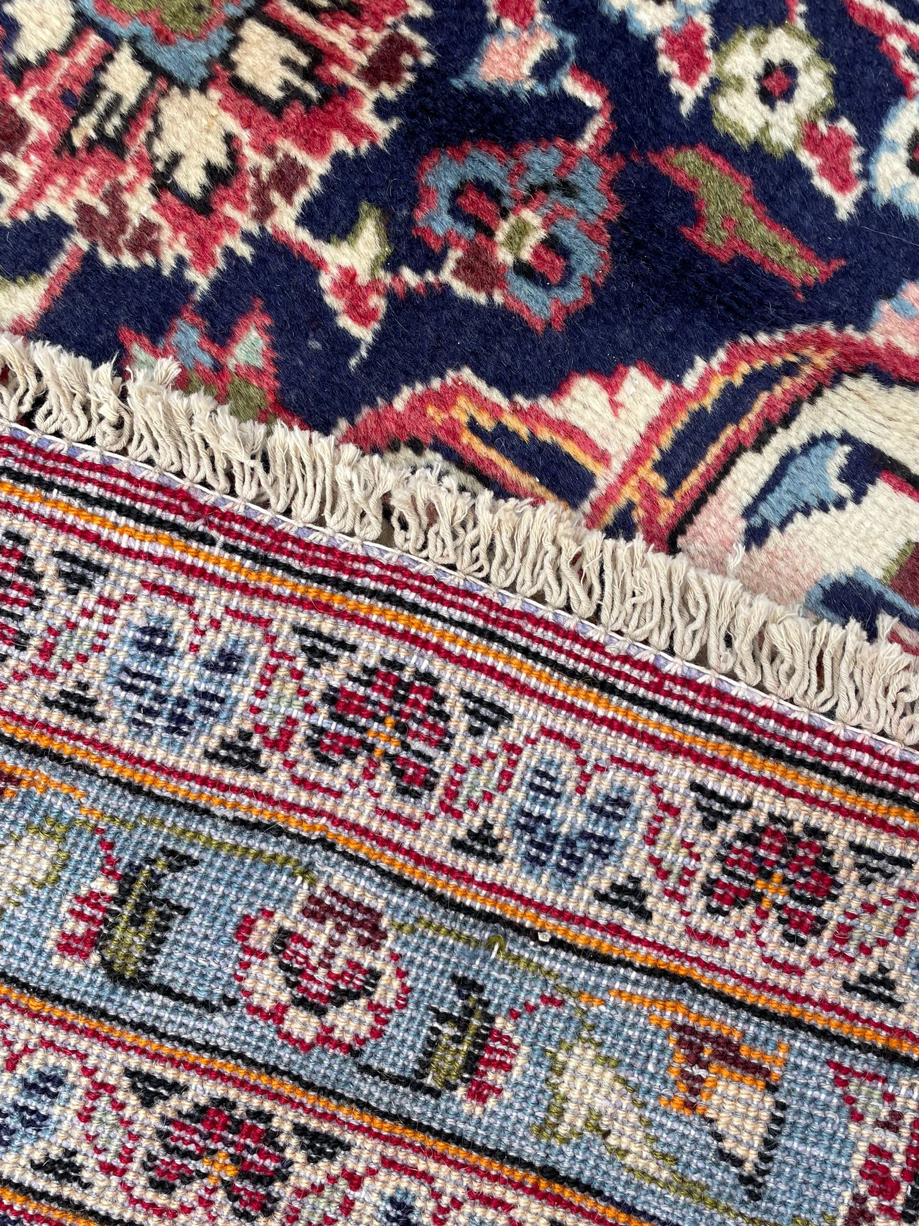 Central Persian Kashan crimson ground carpet, central  floral pole medallion with matching spandrels within a field of scrolling palmette motifs and foliage, the heavily banded indigo border with repeating plant motifs interlaced with scrolled branches