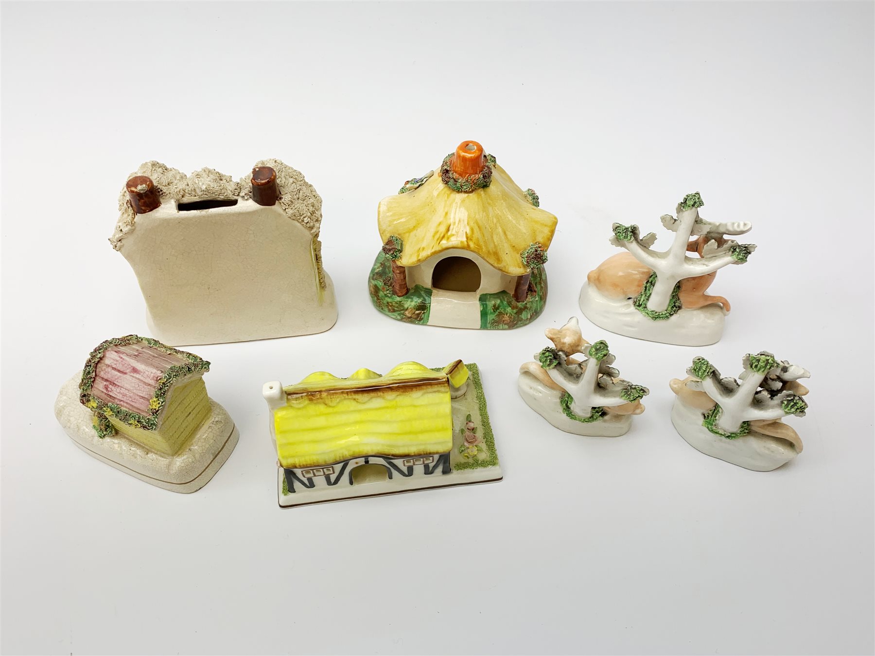 A group of Victorian and later figures, comprising Victorian Staffordshire money box in the form of a house, a Victorian Staffordshire pastille burner in the form of a house, three figures modelled as recumbent deer before trees, Staffordshire style model of a dog emerging from a kennel upon pen holder base, and Coalport pastille burned in the form of a house. (7). 