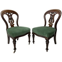 Pair of Victorian mahogany dining chairs, moulded balloon back with scrolled and pierced splat with central shield, upholstered in green fabric, on turned and fluted front supports with brass cups and castors 