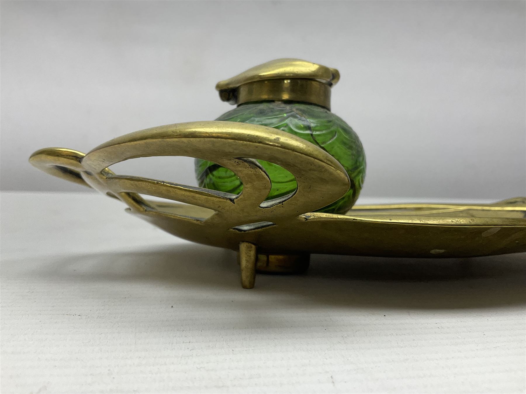 Art Nouveau Geschutzt brass desk stand, with stylised whiplash relief decoration, with removable Loetz style green glass inkwell, stamped to the base, H8cm