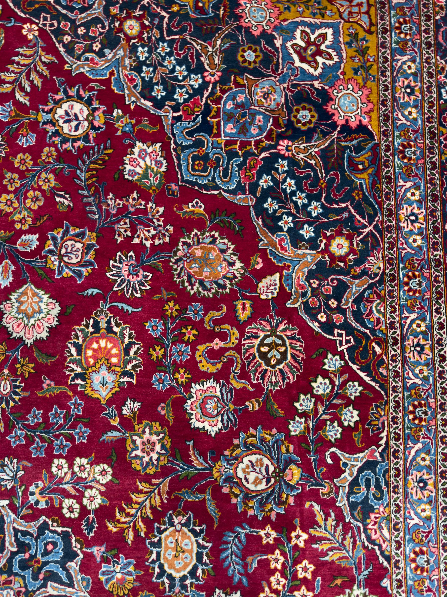 Central Persian Kashan hand-knotted carpet, madder red field with an intricate design of scrolling vines, palmettes, and rosettes with a central lobbed medallion with pendant motifs in shades of blue and ivory, and spandrels all within a blue-ground border of palmettes and flowerheads between multiple guard borders, 450cm x 335cm 