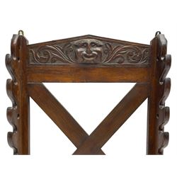 Victorian oak wall hanging whip or stick rack, sloped arch pediment carved with central grotesque mask with extended scrolling foliage, the upright supports cut with rests, x-framed back, two lower hooks