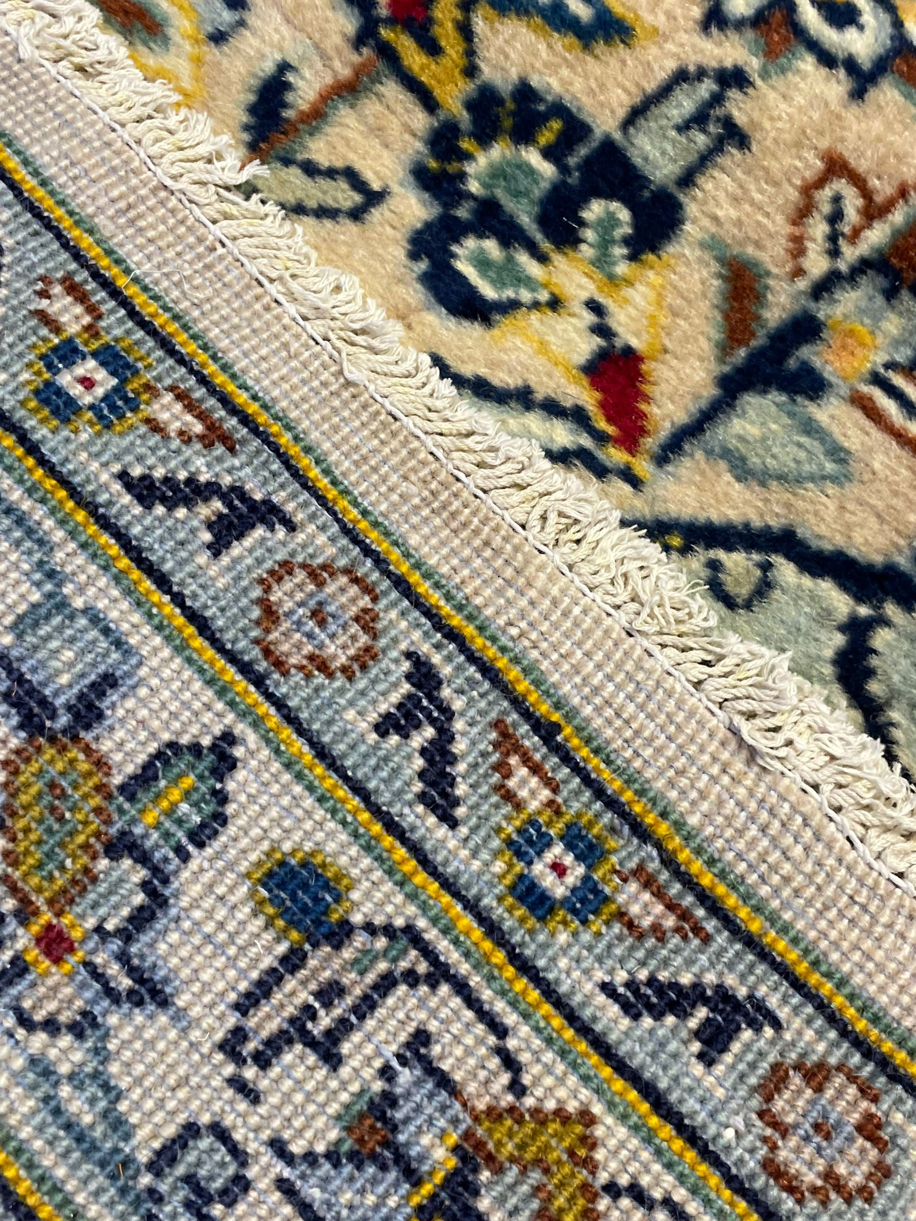 Central Persian Kashan pale khaki ground carpet, shaped central medallion enclosing small stylised motifs, the field decorated profusely with trailing foliate branches and plant motifs, guarded border with repeating floral design 