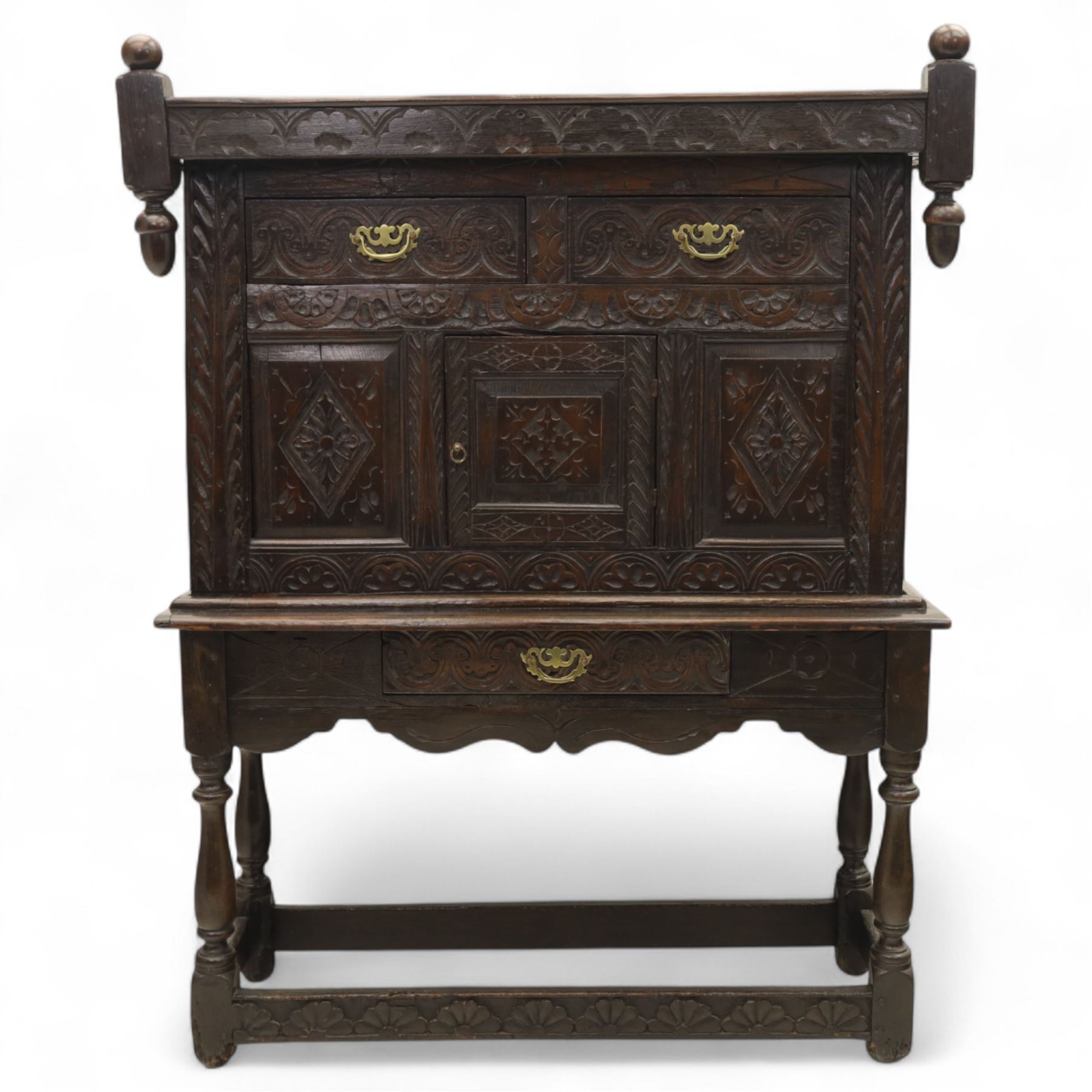 19th century and later carved oak court cupboard, the upper section with two drawers above a central cupboard door flanked by panels, lower section with single long drawer, on turned supports united by carved stretchers