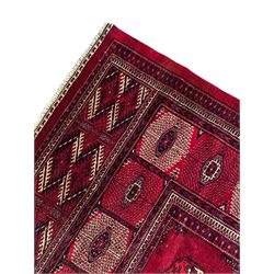 Afghan Bokhara red ground carpet, the field decorated with four rows of Gul motifs interspersed with Hac motifs, the border with lattice pattern panels within small geometric guard stripes, geometric patterned end panels