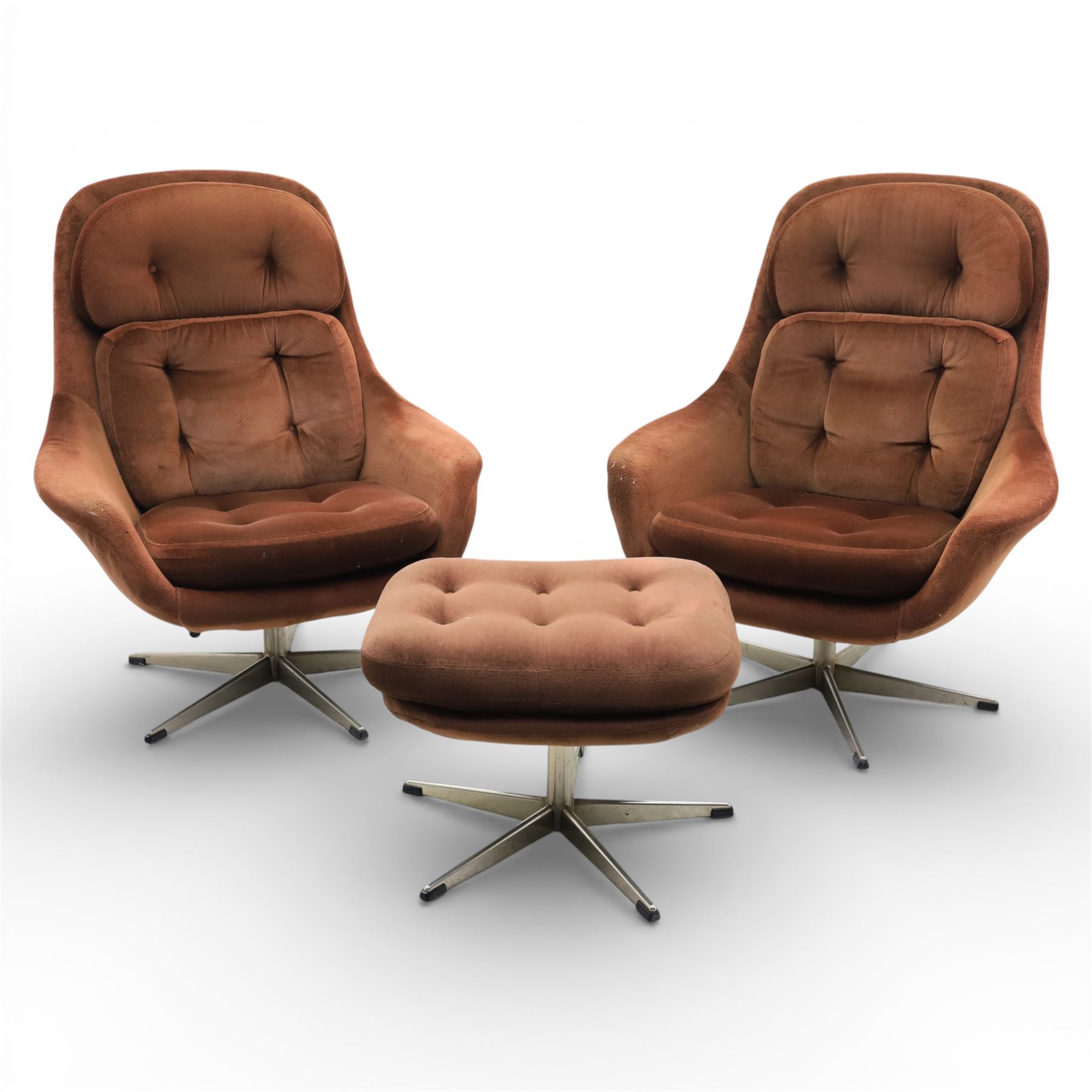 Pair of mid 20th century brown velvet swivel lounge chairs and matching footstool, the shaped and padded back with buttoned segmented cushion over conforming seat cushion, flared armrests and moulded sides, raised on a five point metal swivel base, the footstool en suite with buttoned cushion and matching metal base