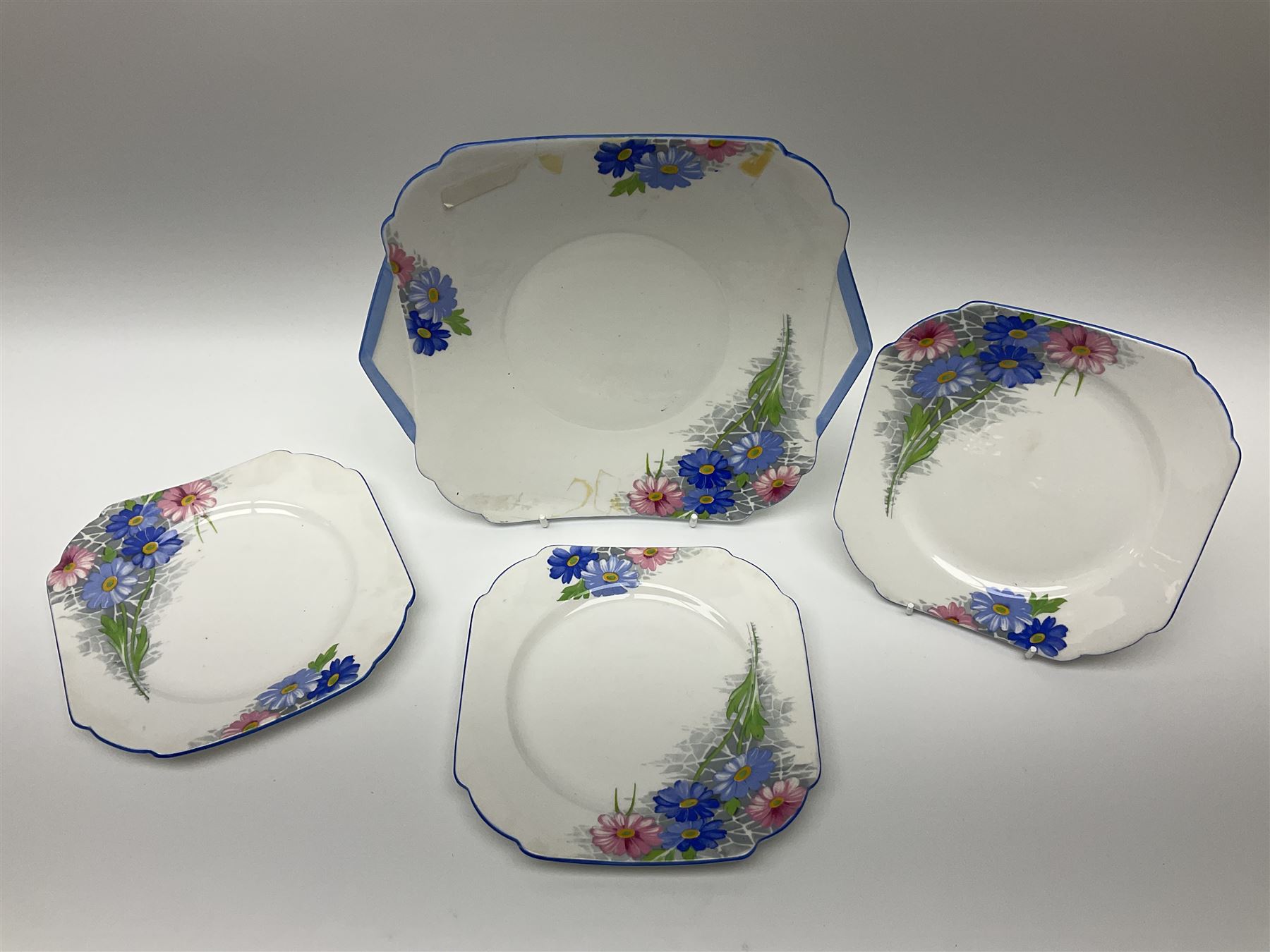 Shelley Strand shaped tea wares, decorated with blue and pink daisies upon a white ground, comprising four teacups, four saucers, three tea plates, milk jug, sugar bowl and cake plate, all with printed green mark beneath and painted pattern no 12216