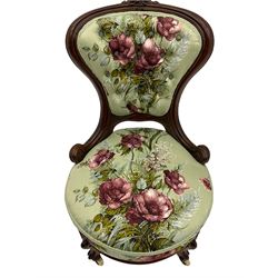 Victorian walnut framed nursing chair, spade shaped back carved with flower heads, upholstered in buttoned rose patterned fabric, on scroll carved cabriole supports terminating at brass and ceramic castors