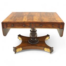 Regency rosewood sofa table, rectangular top with variegated rosewood veneers, hinged D-shaped leaves, over a set of dummy drawers to the back and full-size drawers to the front, with turned knob handles and gilt beaded moulding on frieze above elegant turned, tapering, and fluted, pedestal with a well-carved collar, supported on a large, tripartite concave platform base terminating in richly carved lion paw feet with gilded acanthus leaf carving, on concealed brass castors, circa 1815, length extended 161cm 
