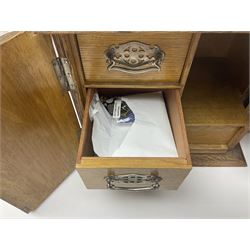 Early 20th century oak smokers cabinet, with brass shield shaped mounts, opening to reveal a compartmentalised interior with three drawers, pipe rack and tobacco jar, together with a small wooden shelf, smokers cabinet H28.5cm