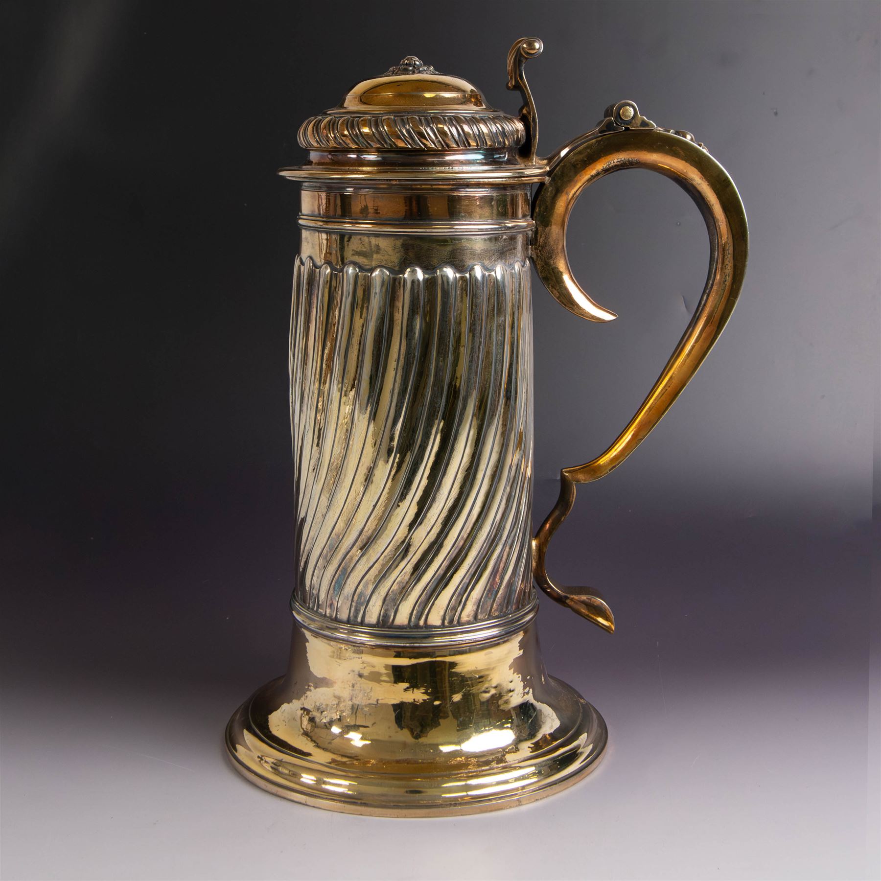 George I silver-gilt wine flagon, of tapering cylindrical form with part fluted body and upon circular spreading foot, with c-scroll handle, domed lid with rose to centre  and scroll thumb piece, hallmarked London 1725, maker's mark indistinct, with later refinements, the original hallmarks struck-through and re-assayed by the London Assay 2021, H33cm